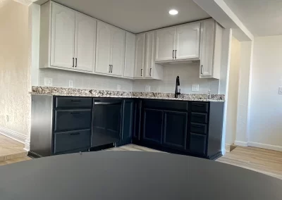 A sleek kitchen featuring white upper cabinets and dark lower ones, complemented by marble countertops and a black faucet under bright lights. For those seeking to match interior elegance with exterior charm, Alpha Omega Finishers is the painting company trusted for top-tier results.