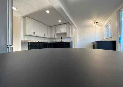 Modern kitchen with white cabinets, black appliances, and recessed lighting, viewed from a low angle near a table. A skilled painting company has ensured every surface shines with perfection, adding an extra touch of elegance to the space.