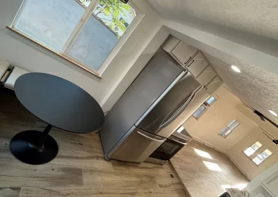 Modern kitchen with wood flooring, a stainless steel fridge, round black table, and large windows—a space where expert interior painters have ensured that every wall complements the sleek design.