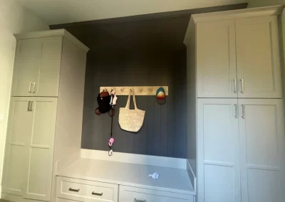 Entryway with a built-in bench, hooks holding bags and hats, and cabinets on each side against a freshly painted paneled wall by our expert painting company.