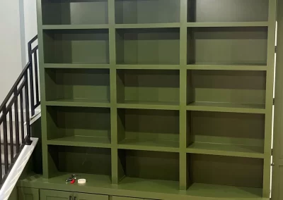 A green built-in bookshelf with multiple shelves and cabinets below graces the space by the staircase, a masterpiece by skilled interior painters.