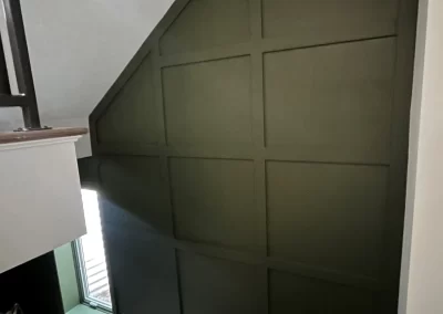 Dark green paneled wall done by Alpha Omega Finishers graces the staircase beside a small window.