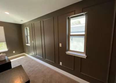 Room with dark paneled walls, beige carpet, and two windows with shelves, allowing natural light to enter—a perfect canvas for any skilled interior painter.