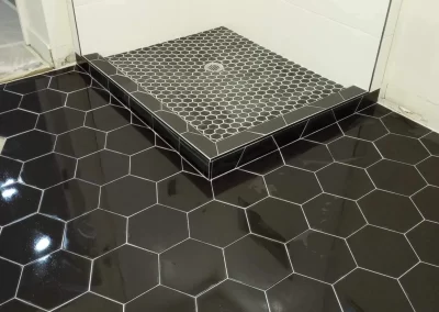 The bathroom features black hexagonal floor tiles and a small raised shower area with stylish black and white hexagonal tiles, expertly finished by our top-rated interior painters.