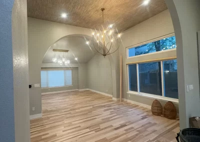 Spacious room with wooden floor, high ceiling, modern chandeliers, large windows, and arched doorways, enhanced by the expert touch of Alpha Omega Finishers.