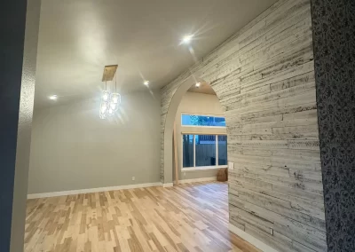 Room with hardwood floor, light fixture on the ceiling, wooden accent wall, and an arched opening to another space crafted with care by Alpha Omega Finishers.