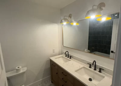 Modern bathroom with dual sinks, black fixtures, a large mirror, warm lighting, and hexagonal floor tiles beautifully complemented by expertly chosen hues from skilled interior painters.