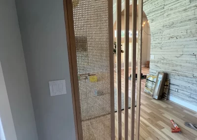 Wooden partition with a woven cane design separates spaces in a room with light wood flooring and textured walls, showcasing the attention to detail that Alpha Omega Finishers is known for.