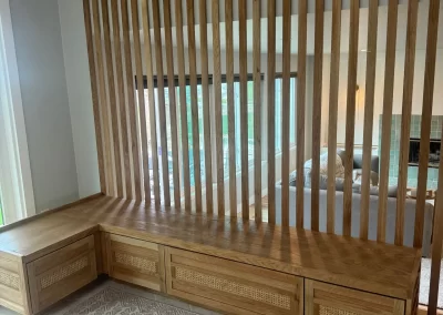 Wooden slatted room divider with built-in bench and storage, expertly crafted by Alpha Omega Finishers, sits next to a window and patterned rug.