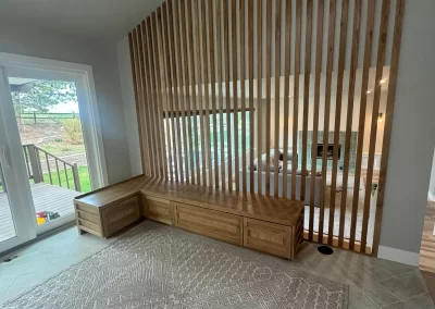 Modern room with a slatted wooden divider, built-in bench with drawers, and a patterned rug by renowned interior painters. Large glass doors open to a deck.