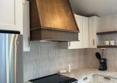 Modern kitchen with stainless steel appliances, white cabinets, wooden range hood, and a coffee maker on the counter all glisten as if touched by a master painting company.