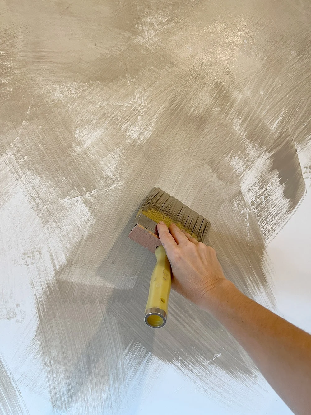 Hand painting an exterior Limewash Walls beige with a wide brush, creating textured strokes, showcases the precision that Alpha Omega Finishers, a renowned painting company, is known for.