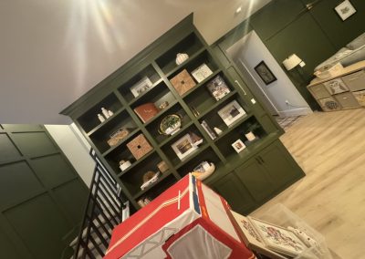 Dark green built-in shelves display decor items in a cozy, well-lit living space with wood flooring.