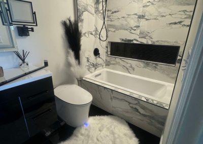 Modern bathroom with marble walls, white tub, black fixtures, and a fluffy white rug on a dark floor.