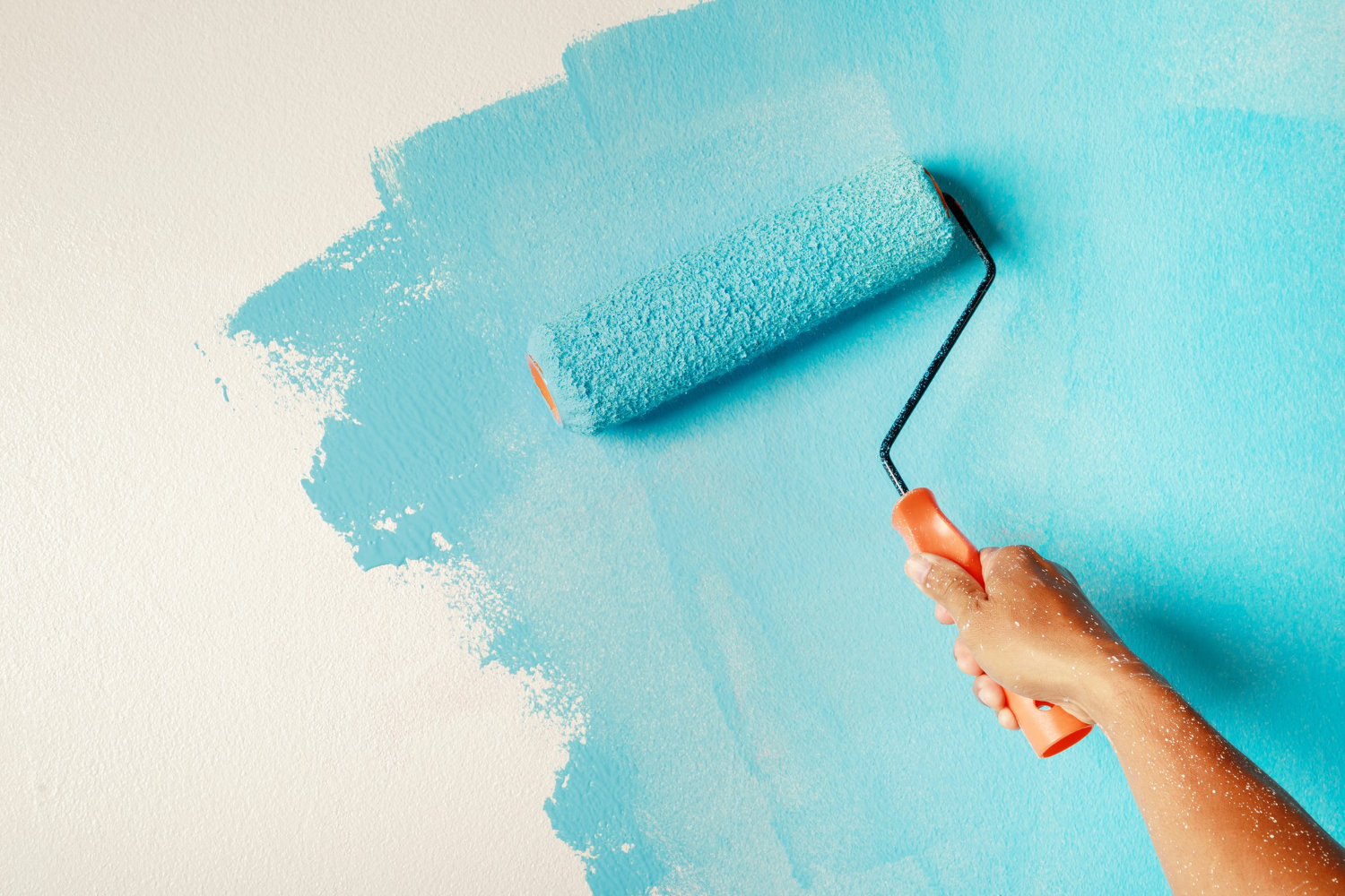 2098 A hand painting a white wall light blue with a paint roller.