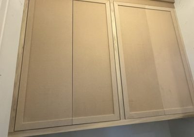 Unfinished wooden cabinets above a sink with tools and construction materials on the counter.