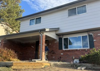 Two-story brick and white house with front porch, steps, and a person standing near the entrance.
