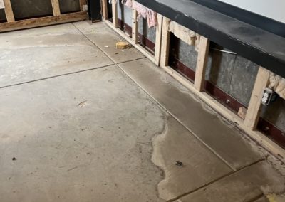 Exposed wall framing and wet concrete floor, showing signs of recent water damage in a room under repair.