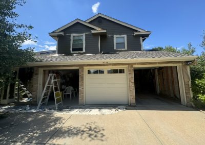 Two-car garage of a house, with one door open, ladders outside, and renovation materials visible.