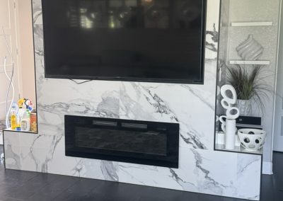 A large TV and modern fireplace on a marble wall with decorative shelves and contemporary decor items.