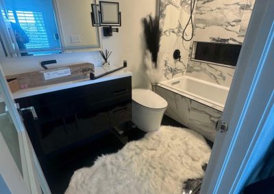 Modern bathroom with black and white decor, marble walls, and a fluffy white rug on the floor.