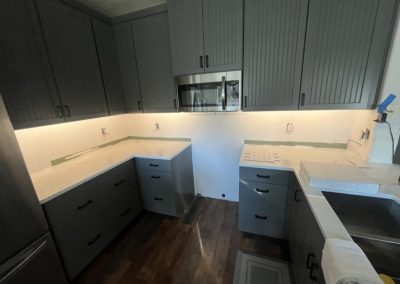 Modern kitchen with gray cabinets, under-cabinet lighting, and unfinished countertops.