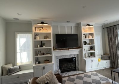 Living room with built-ins, a TV above a fireplace, shelves with decor, and window seats on each side.