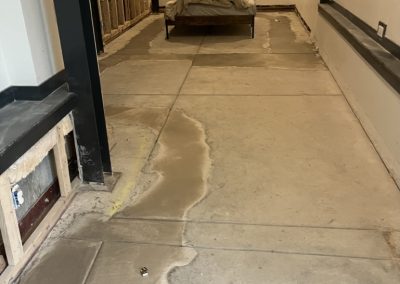 A basement room with exposed wall studs, concrete floor, and a covered bed at the far end.