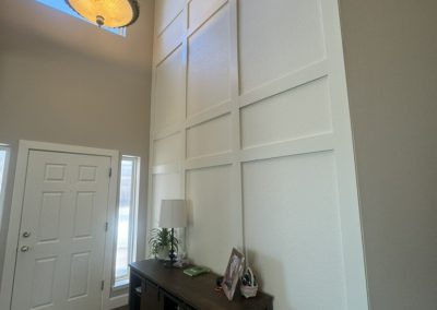 Tall white entryway with a grid accent wall, side table, and hanging light fixture.