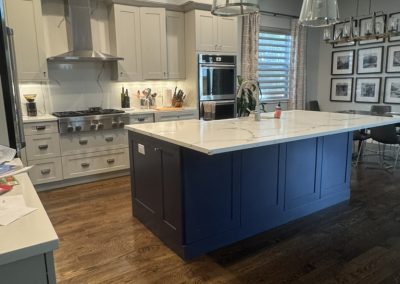 Modern kitchen with white cabinets, blue island, wooden floor, pendant lights, and photo wall display.