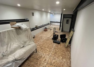 Basement room under renovation with unfinished flooring, tools, and covered furniture visible.