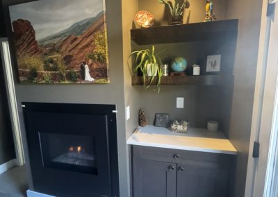 Dark corner nook with fireplace, shelves with plants, decor, and a photo of red rock landscape above.