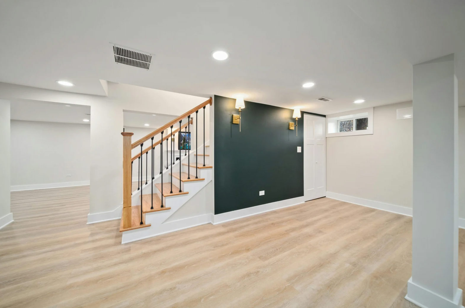 Modern Basement Finishing with wood stairs, green accent wall, and light wood flooring.