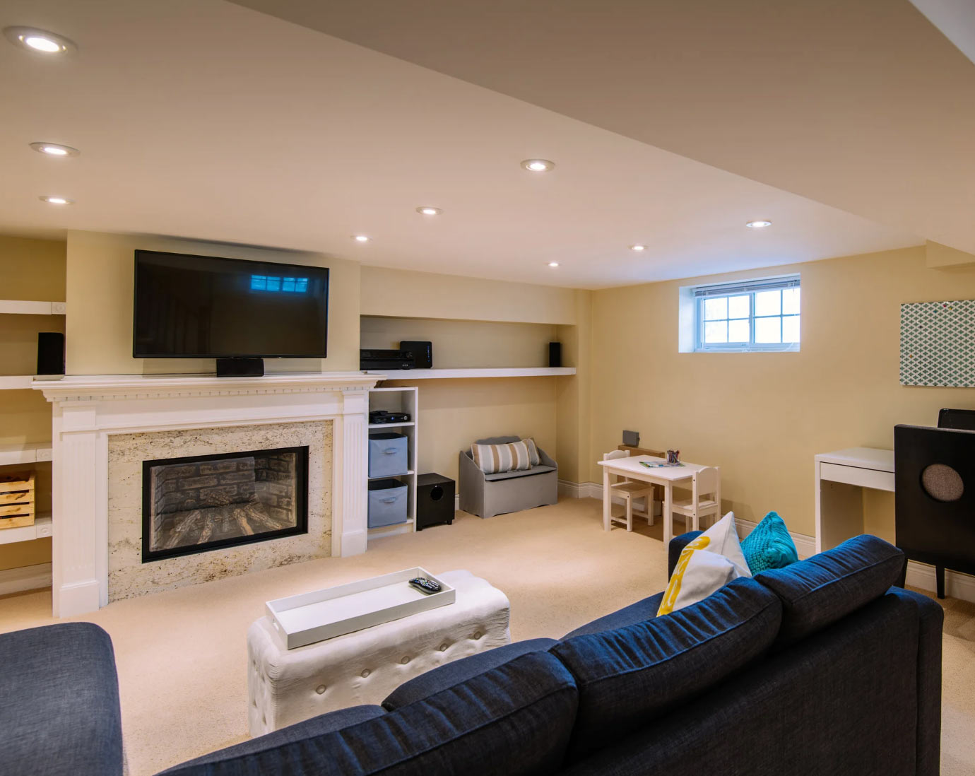 Modern basement living room with a fireplace, TV, sofa, small table, and window letting in light.