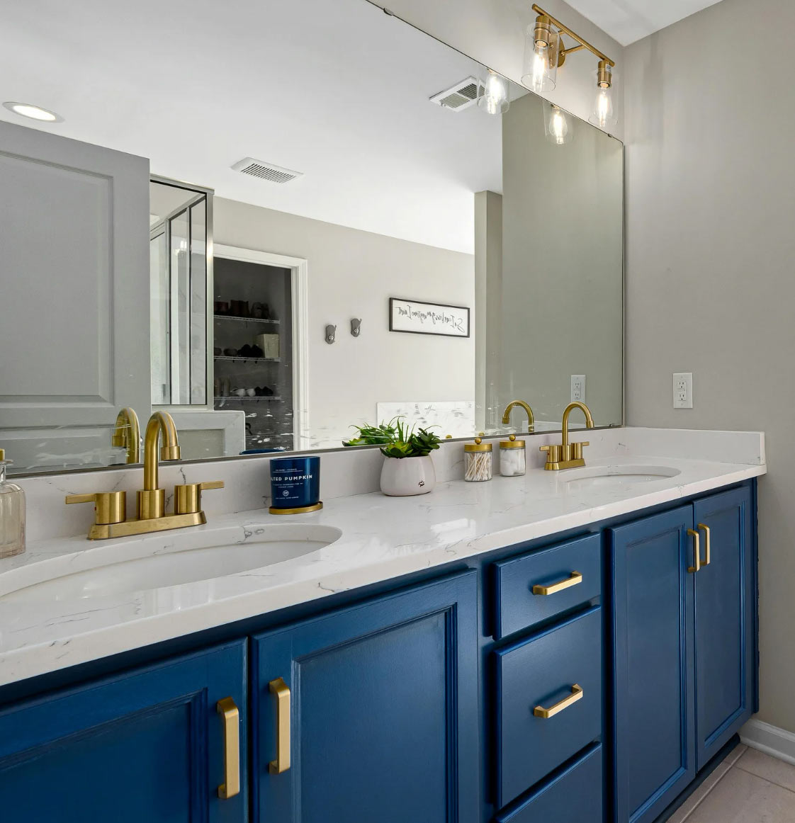 Modern bathroom with blue cabinets, gold fixtures, double sinks, large mirror, and neutral walls.